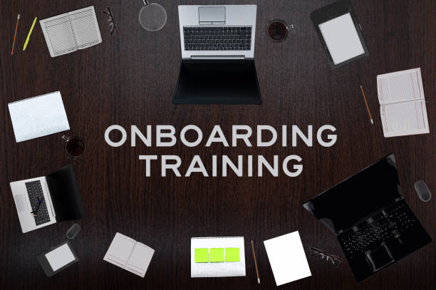 Top view of Onboarding training text on the table with laptops, notepad, coffee, eyeglasses, pens. Business concept.